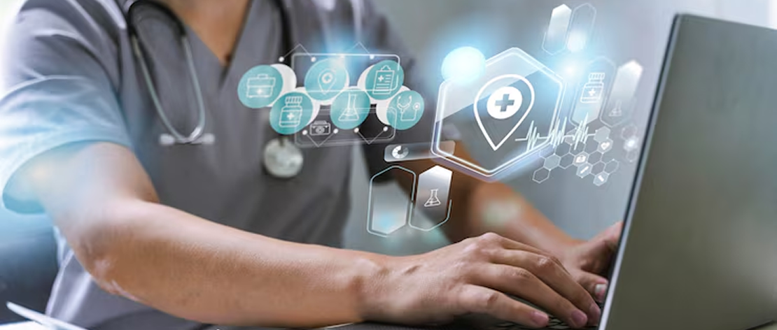 A doctor in a white coat types on a laptop displaying a medical history form. The desk holds medicine bottles, a blood pressure monitor, and medical tools